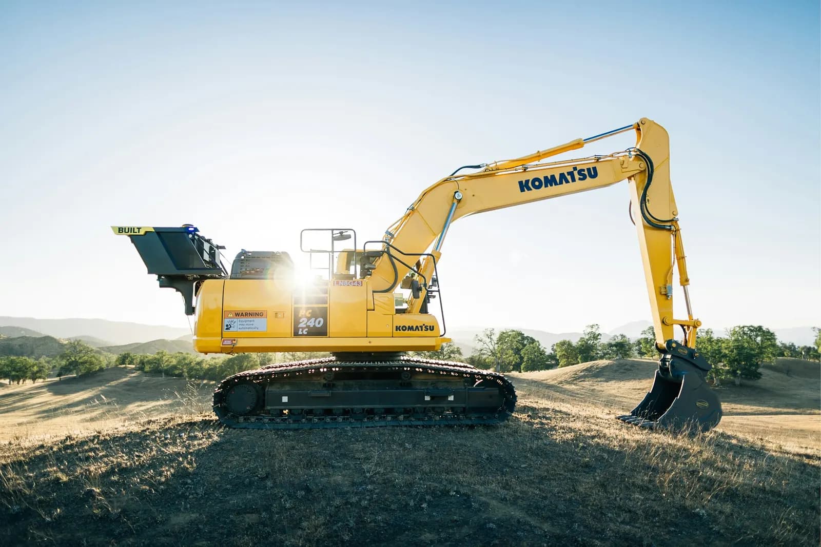 Yellow excavator on a dirt rise at sunrise